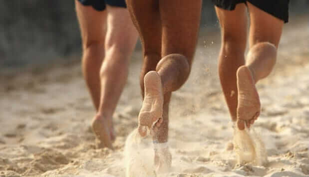 A group of men on barefoot running stride on the beach